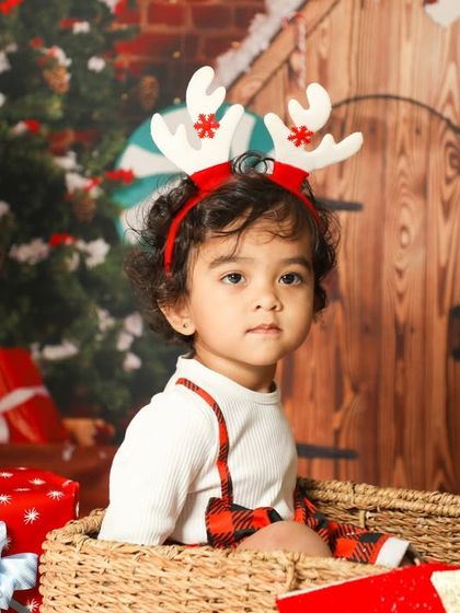 Hey there, little reindeer! This toddler looks so festive and ready for Christmas in this cozy basket setup with lots of presents.