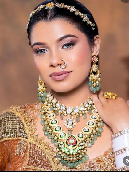 A close-up of a bride wearing a stunning layered bridal necklace with mint green stones and intricate polki work. The set includes a matching sheesh patti and nath for a complete, regal look.