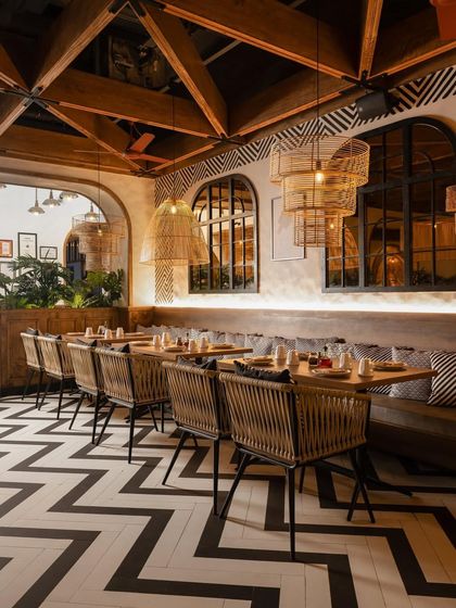 The restaurant's design is a masterclass in pattern and texture, with bold chevron flooring, hand-painted wall motifs, and woven dining chairs.