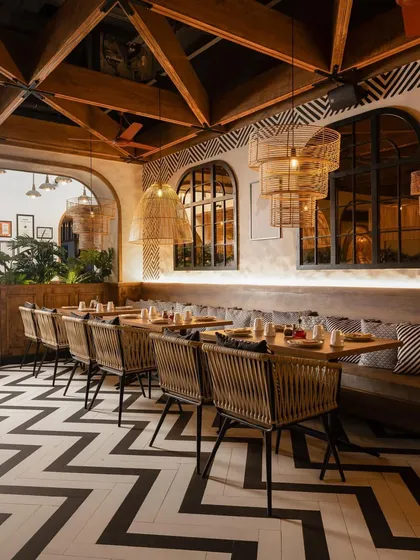 The restaurant's design is a masterclass in pattern and texture, with bold chevron flooring, hand-painted wall motifs, and woven dining chairs.