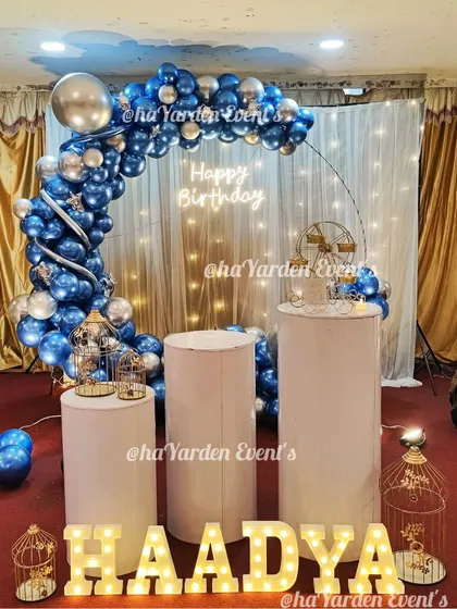 A half-ring balloon arch in blue and silver against a lit curtain, creating a glamorous effect.