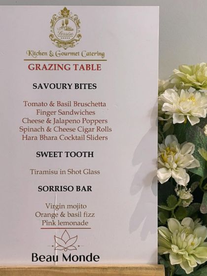 The custom grazing table menu for the Beau Monde Clinics event. The menu lists a variety of savory bites, sweets, and drinks, all carefully selected for the occasion.