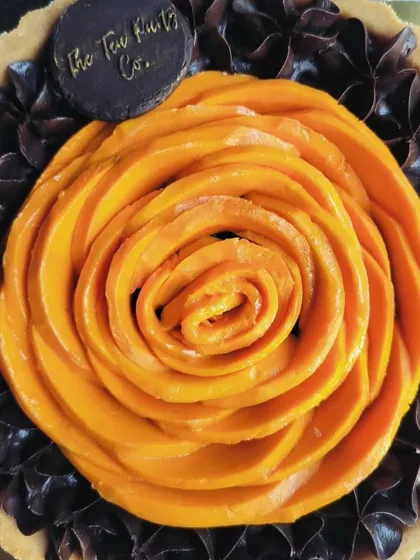 A close-up of the mango rose, crafted from fresh mango slices, sitting atop a bed of decadent dark chocolate piping.
