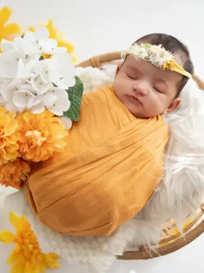 A newborn wrapped in a warm yellow swaddle, resting in a basket with matching flowers. We coordinate colors and props to create a cohesive and artistic final image.