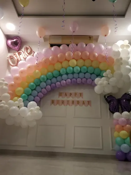 A pastel rainbow balloon arch for a first birthday. This softer take on the rainbow theme uses gentle colors and includes a butterfly balloon pillar, creating a dreamy atmosphere.