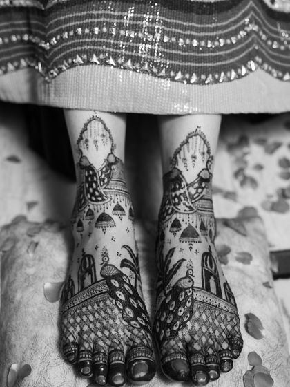 A black and white shot of an intricate peacock design on the feet. The monochrome effect highlights the boldness and clarity of the patterns.