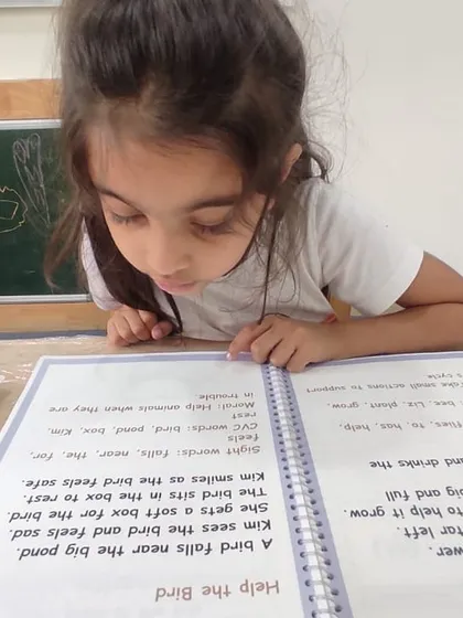 I read, I learn. Our literacy program is designed to build a strong foundation, starting with letter sounds and moving towards independent reading. This student is deeply focused on her reading material, a common sight in our K2 program.