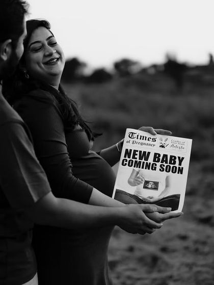 A happy, candid black and white shot of the couple sharing their news with the "Times of Pregnancy" newspaper. Her smile says it all.