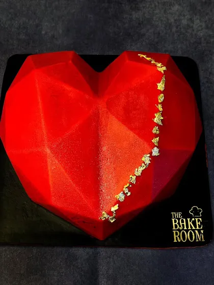 A striking geometric heart-shaped Piñata Cake. The vibrant red shell is decorated with a touch of gold leaf, creating a modern and passionate dessert centerpiece.