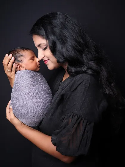 A gentle and intimate portrait of a mother holding her swaddled newborn close. The focus is on the quiet moment and the bond between mother and child.