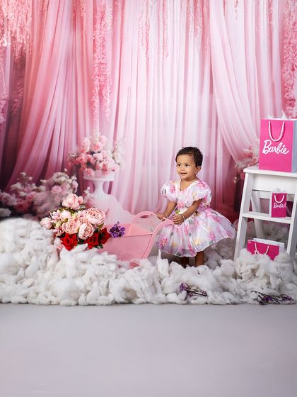 A dreamy Barbie world. This little girl, surrounded by fluffy clouds and pink floral decor, is living her princess fantasy in this beautiful themed shoot.