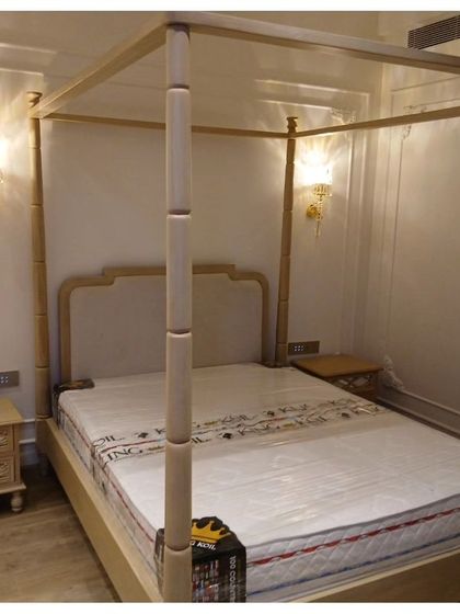 A grand four-poster bed crafted from light-finished wood, featuring intricate detailing on the posts. This piece brings a sense of classic romance and luxury to the bedroom, complemented by ornate wall sconces.