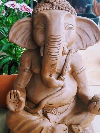 A serene, meditating Ganesha idol made from natural clay, sitting beside a flowering plant.