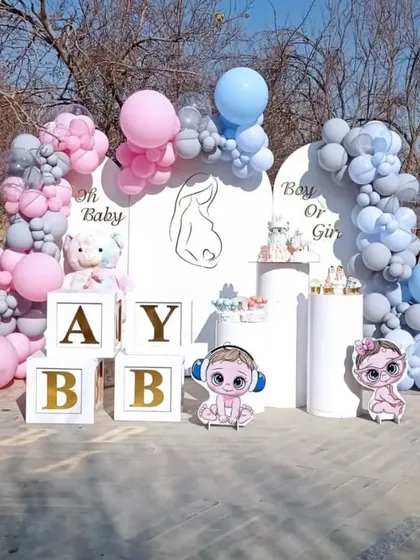 An outdoor 'Boy or Girl' gender reveal party with pink and blue balloon arches, custom backdrops, and 'BABY' blocks.