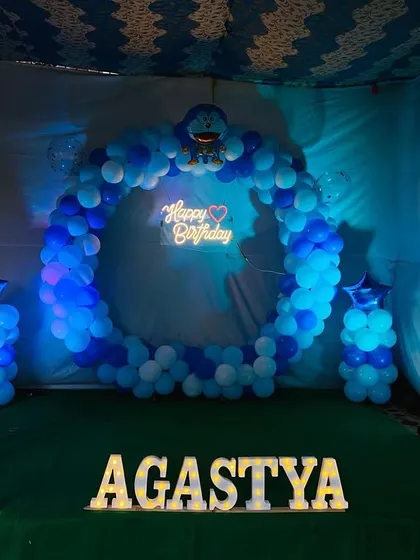 A Doraemon themed first birthday party. The setup includes a circular balloon arch, marquee letters for the name 'Agastya', and character cutouts.