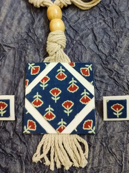 A flat-lay of the blue block-print necklace set, showing the detail of the fabric print and the texture of the macrame cord and tassel.