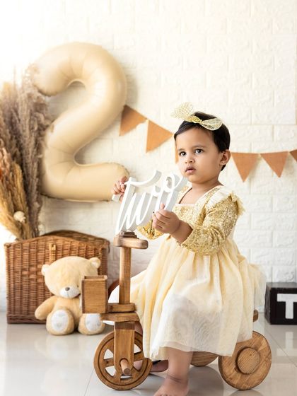 Posing with a wooden tricycle and a 'two' sign, this portrait is full of charm. The props are all child-safe and add a playful element to the shoot.