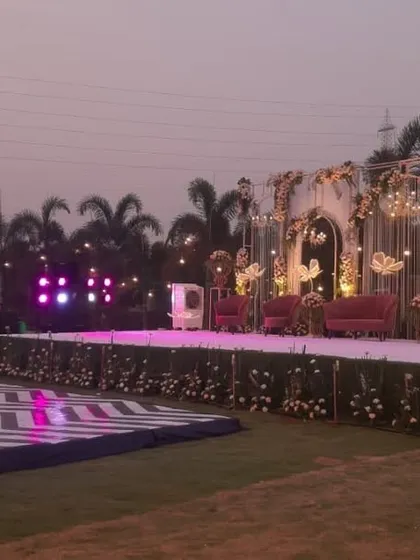 A wide view of a reception stage and dance floor setup at dusk. The elegant white and gold stage is complemented by a modern chevron dance floor, ready for the party to begin.