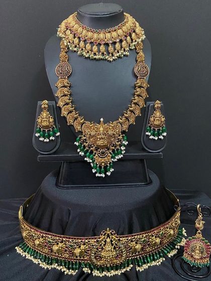 This Nagas bridal set features a bold goddess pendant and green bead detailing. The set includes a choker, long necklace, and a matching vaddanam with elephant motifs.
