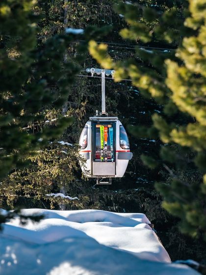A ski gondola, framed by trees, ascends a snowy mountain. A simple, quiet moment that captures the feeling of a day on the slopes.
