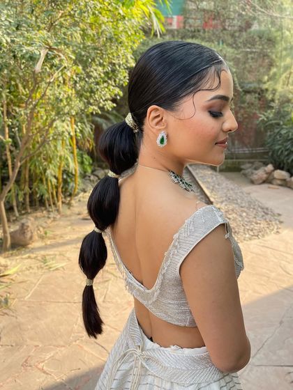 A side view of a sleek bubble ponytail with delicate, curly baby hairs. This is a very trendy and high fashion look.