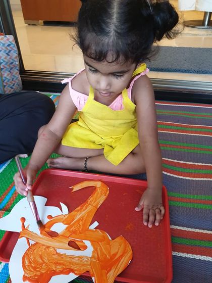 A toddler carefully painting a Ganesha cutout. Our festival workshops are designed to be accessible and fun for even the youngest artists.