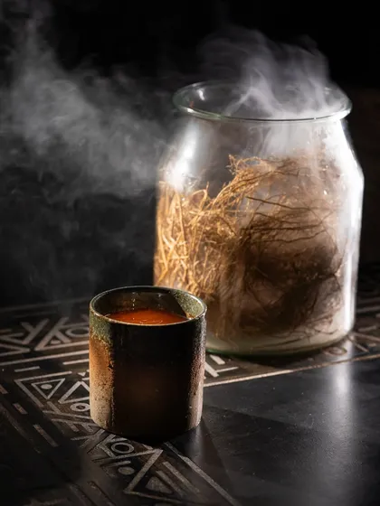 A dark and moody shot of a steaming, spiced beverage. The contrast between the dark background and the rising steam creates a sense of warmth and mystery.