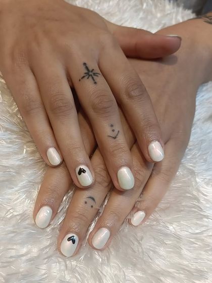 A sweet and subtle design on short, natural nails. This pearly white manicure is personalized with tiny, hand-painted black hearts.