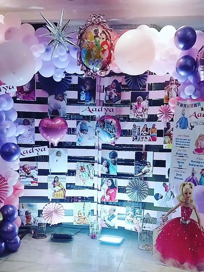 A personalized photo wall is a great way to celebrate memories. For this princess party, I created a custom backdrop with black and white stripes to display photos, framed by a beautiful balloon garland and a life size Barbie doll cutout.
