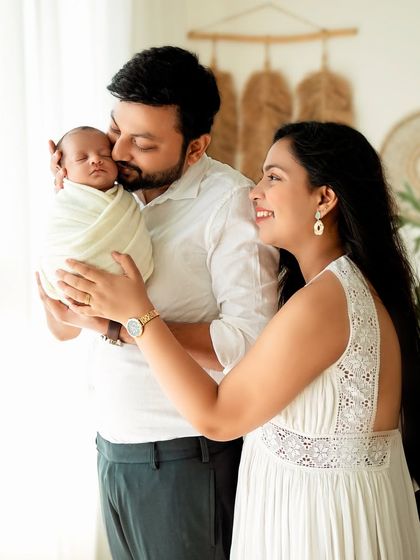 A bright and airy family portrait. The parents are beaming with joy as they hold their swaddled newborn.