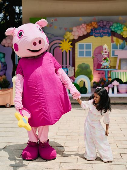 The birthday girl having a wonderful time with the Peppa Pig mascot.
