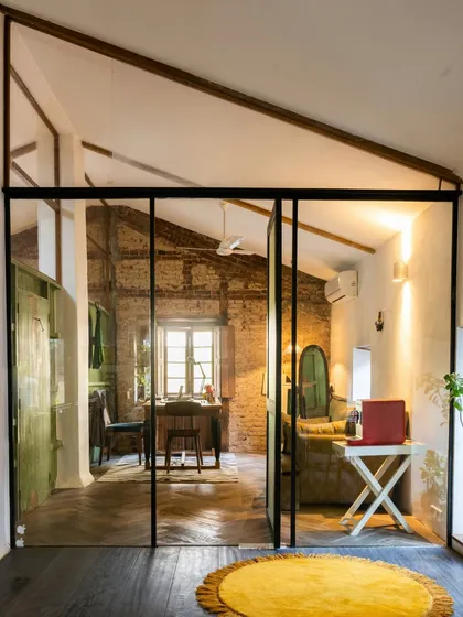 We used glass partitions to create separate zones without sacrificing the open, airy feel of the studio. This view into my office shows how modern elements can coexist with heritage architecture, maintaining a connection to the entire space while providing a quiet work area.