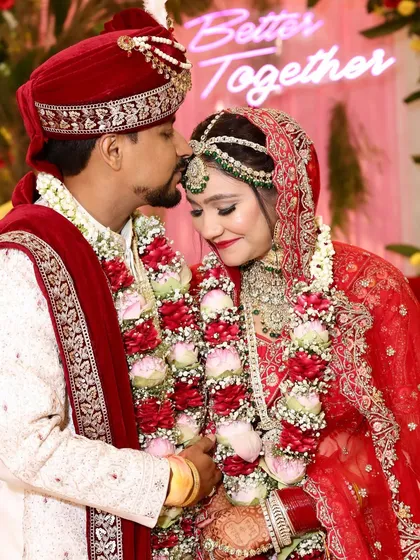 A beautiful moment between the bride and groom. Her classic red lehenga is paired with soft, glowing makeup and green jewelry, creating a timeless and romantic look.