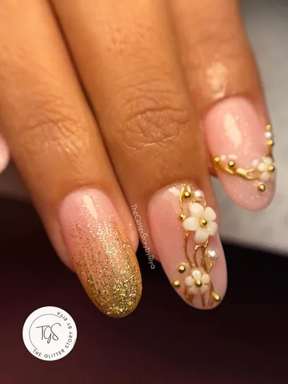 This close-up highlights a gold glitter ombré accent nail paired with delicate 3D floral work. Mixing textures like glitter and sculpted art adds another dimension to a bridal manicure.