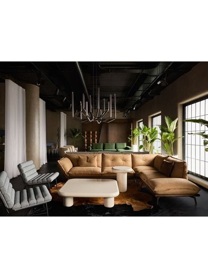 A spacious living room arrangement with a tan leather L-shaped sofa and modern grey armchairs. The use of sheer curtains helps define the space while maintaining an open, airy feel.