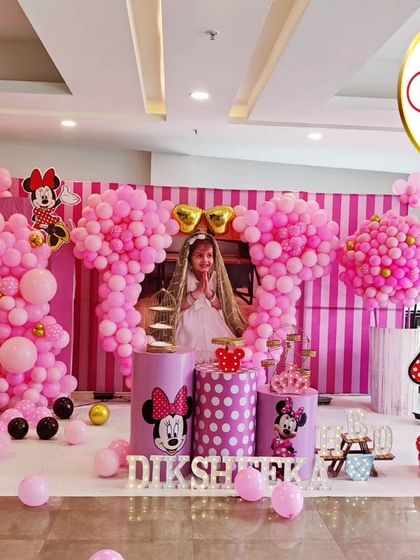 An adorable Minnie Mouse-themed fourth birthday party. This elaborate setup features large, pink, Minnie-shaped balloon sculptures, a striped backdrop, and a photo of the birthday girl.