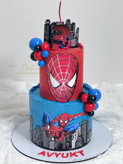 A two-tiered Spiderman cake for a little superhero's birthday. The design features the city skyline, Spiderman's face, and a fun candle placement on top.