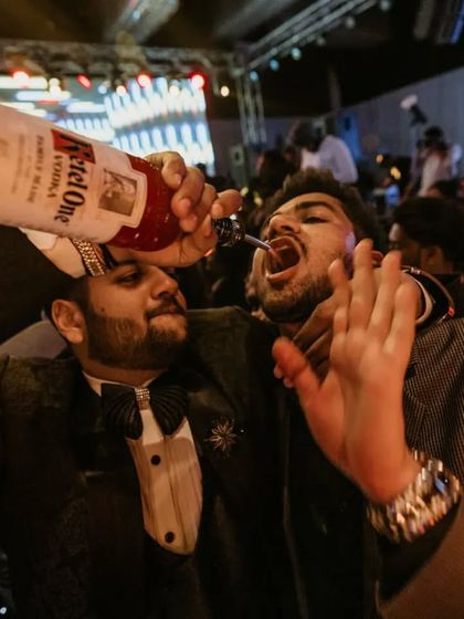 Friends that drink together, stay together. A guest helps his friend take a drink directly from the bottle in the middle of a packed dance floor.