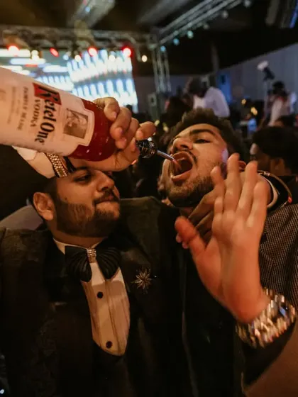 Friends that drink together, stay together. A guest helps his friend take a drink directly from the bottle in the middle of a packed dance floor.