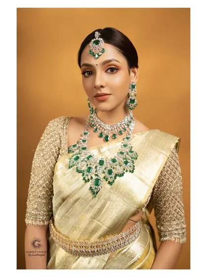 This portrait showcases a natural yet glamorous bridal makeup look. The focus is on enhancing the bride's features with soft, defined eyes and glowing skin, perfectly paired with magnificent emerald jewelry for a touch of royalty.