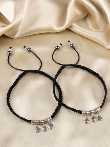 A pair of black cord anklets or bracelets with dangling silver coin charms.