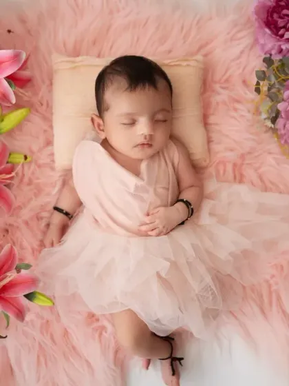 A peaceful newborn portrait with the baby lying on her back, surrounded by beautiful pink flowers. The composition is designed to be soft, serene, and timeless.