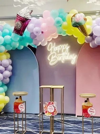 A sweet pastel ice cream themed birthday party. The setup features a colorful balloon arch with ice cream cone balloons and a neon 'Happy Birthday' sign.