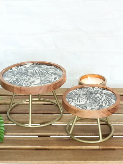 Our Moon Ray serving stands, featuring a wooden base with a monochrome leaf print and a gold metal frame. Available in two sizes, they offer a chic blend of natural and modern design.