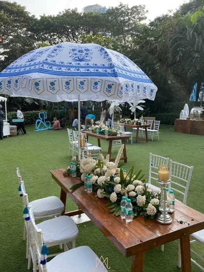 Long wooden tables for guest dining, shaded by beautiful custom-printed umbrellas that match the blue and white theme.