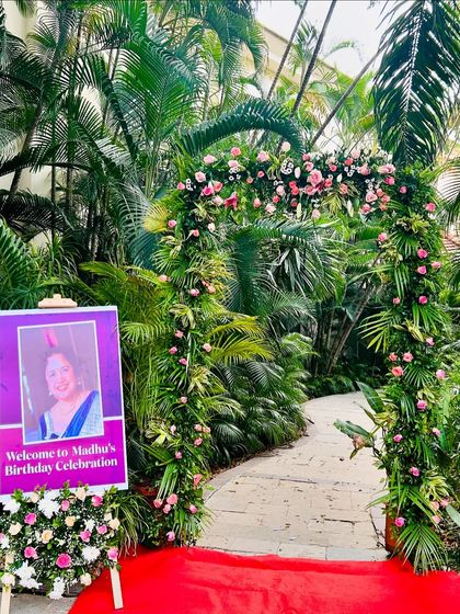 A lush floral arch and red carpet create a grand entrance for a tropical-themed birthday celebration.