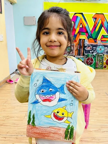 Look at this proud artist with her fantastic shark drawing! Our creative art sessions are all about letting kids explore their imagination and express themselves through color and paint, no matter how messy it gets.