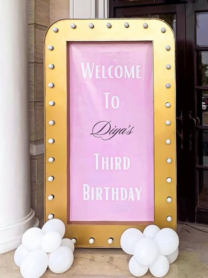 A close-up of the elegant welcome sign for Diya's third birthday. The combination of the gold marquee frame and simple balloon accents is both chic and festive.