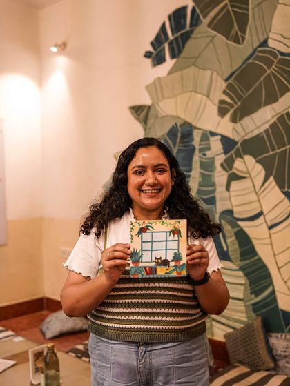 A participant shows off her creative painting of a cat surrounded by plants.