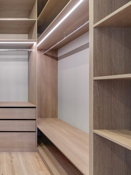Another angle of the light oak laminate closet interior, showcasing the combination of drawers, open shelving, and a bench area, all designed for maximum utility.
